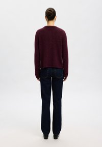 Maroons vērpjuma vilnas džemperis ar noapaļotu kakla izgriezumu, apvienots ar tumši zilām taisnām biksēm. Gluda tekstūra ar minimāliem dizaina elementiem.