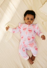 Tutina a quadretti viola e rosa con motivi a cuore e scritta "DADDY". Presenta rifiniture bianche e maniche con volant. Il bebè tiene una coperta di colore chiaro.