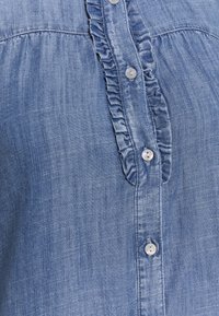 Camicia di jeans azzurro chiaro con placca arricciata e bottoni perlati, con una morbida texture e sottili linee verticali.