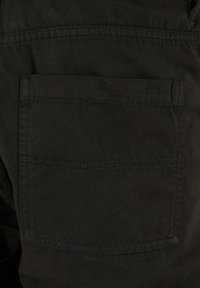 Pantalons en tissu noir avec une poche arrière unique dotée de détails de couture visibles. La texture semble lisse avec une finition mate.