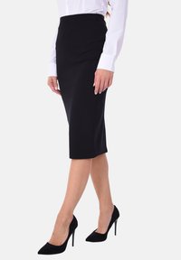 Gonna a matita nera realizzata in tessuto elastico, di lunghezza al ginocchio con una texture liscia e una silhouette aderente, abbinata a scarpe con tacco alto nere.