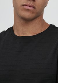 Svart T-skjorte med en teksturert stripete design, rund hals og korte ermer. Stoffet ser mykt ut med subtile variasjoner i tone.