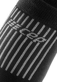Zwart compressiesok met grijze verticale strepen. Gemaakt van gebreid materiaal met een logo en een textuurstof voor verbeterde grip.
