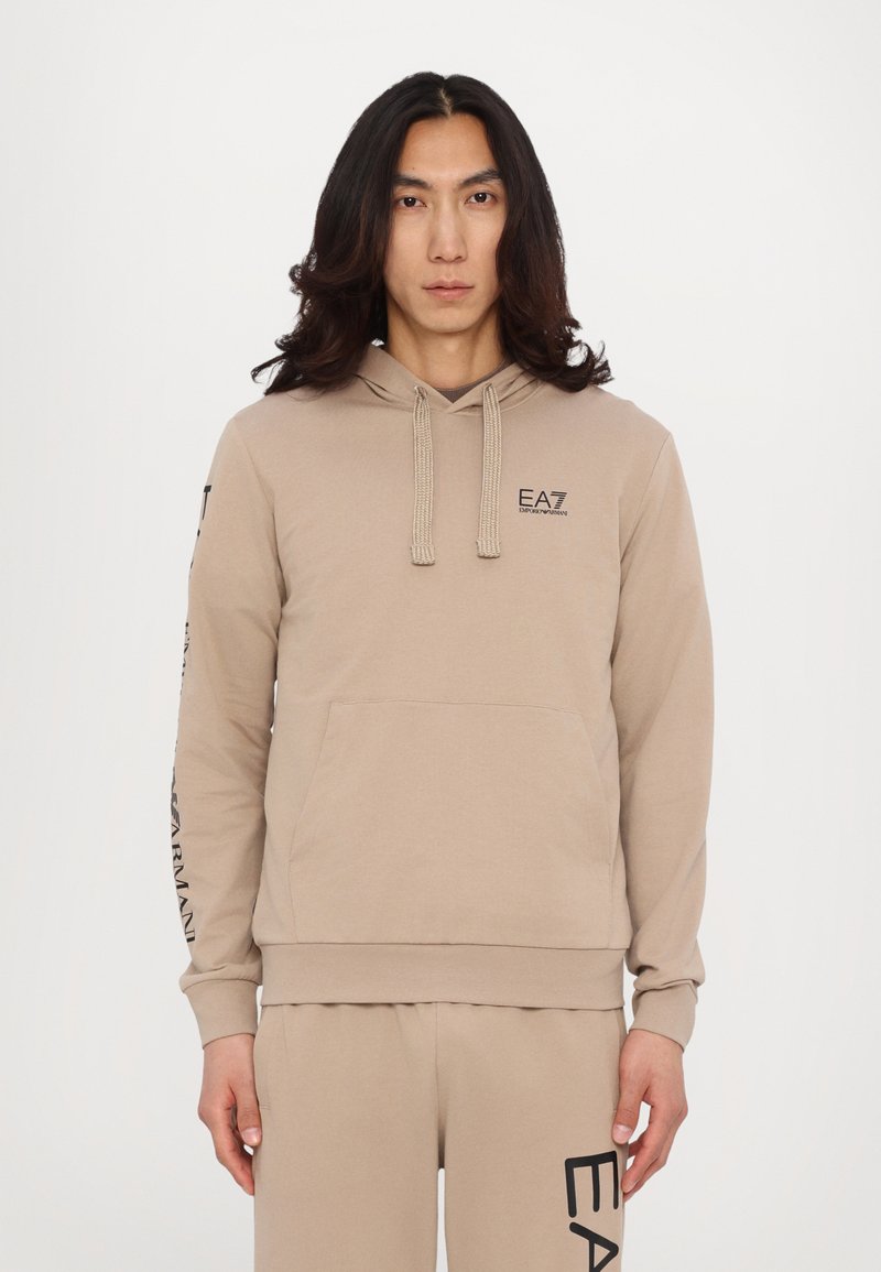 Felpa beige in misto cotone, con tasca frontale, cappuccio con coulisse e logo stampato sul braccio. Abbinata a pantaloni coordinati.