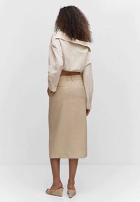 Chemisier court beige avec un grand col, associé à une jupe beige taille haute. La jupe présente une silhouette droite et des poches arrière.