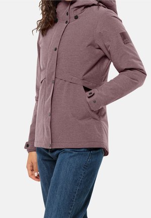 Mujer con chaqueta con capucha morada, botones en el frente y bolsillos laterales, combinada con vaqueros azules, sobre un fondo liso.