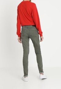 Punainen pitkähihainen paita, oliivinvihreät slim-fit-housut, valkoiset lenkkarit. Yksinkertainen muotoilu ilman kuvioita, tavanomainen rento istuvuus ja klassiset värit.
