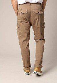 Tan cargobroeken met meerdere zakken, een elastische tailleband en opgerolde mouwen, gecombineerd met beige sneakers met zwarte accenten.