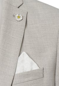 Lichtgrijze textuurblazer met een witte pochet met een subtiel bloempatroon. Accent van een witte en gele madeliefjes-speld op de revers.