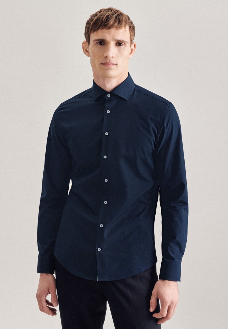 Camicia a maniche lunghe blu navy in tessuto liscio, con colletto classico e sei bottoni bianchi nel davanti, vestibilità aderente con orlo arrotondato.
