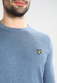 Maglione azzurro chiaro a girocollo realizzato in materiale a costine, con un piccolo logo di un'aquila gialla e nera sulla parte sinistra del petto.