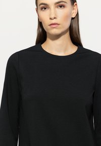 Schwarzes Langarmoberteil mit rundem Ausschnitt. Glatte Textur, taillierte Silhouette und minimalistisches Design ohne Muster oder Akzente.