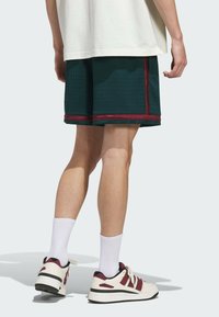 Green mesh basketball shorts with maroon side stripes, flat hem, and a textured surface, paired with white crew socks and red-accented sneakers.