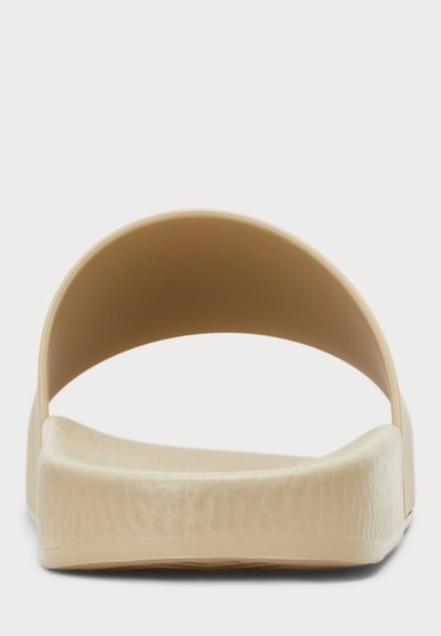 Beige slip-on szandál széles, ívelt pánttal, texturált talprésszel és tömör, lapos talppal. Letisztult, minimalista dizájn, látható fémrészek nélkül.