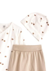 Haut à manches longues blanc avec un design tacheté de beige, pantalon beige assorti avec une taille élastique, et un chapeau blanc avec des taches beiges. Matériau en coton doux.