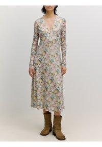 Blumenkleid in Pastellfarben mit tiefem V-Ausschnitt und langen Ärmeln; präsentiert eine Kombination aus pinken, gelben und blauen Blumen; kombiniert mit braunen Stiefeln.