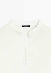 Vit skjorta med krage och knappstängning samt framplacket, tillverkad av slätt tyg. Har en minimalistisk design och subtila söms detaljer.