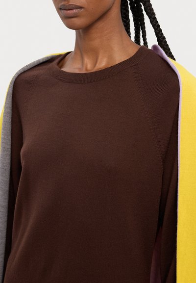 Pull en tricot marron à col rond, avec des accents gris et jaune drapés sur les épaules, mettant en valeur une texture lisse.