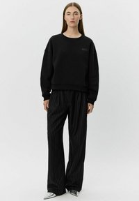 Hanorac negru cu decolteu rotund și logo subtil "oui", asortat cu pantaloni largi negri cu dungi și pantofi metalici cu vârful ascuțit.