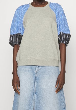 Personne portant un haut gris clair avec des manches bouffantes rayées bleu et noir et une jupe en jean bleu clair.