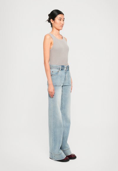 Un débardeur gris à côtes associé à un jean bleu clair à jambes larges, agrémenté d'une ceinture tressée bleue, le tout complété par des chaussures à plateforme noires.