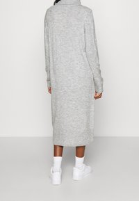 Lungo vestito in maglia grigia con colletto e polsini a coste, caratterizzato da un taglio dritto che arriva a metà polpaccio. Indossato con sneakers bianche.
