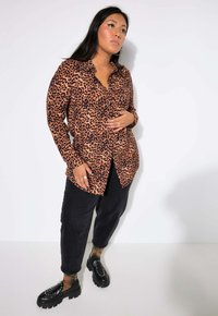 Camicia a maniche lunghe con stampa leopardata in tonalità di marrone e nero, abbinata a pantaloni neri a sigaretta e scarpe nere massicce. Tessuto morbido.