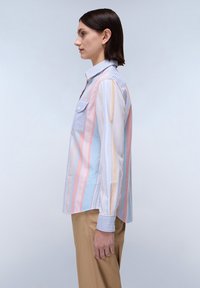 Camicia a righe nei colori pastello con una combinazione di motivi verticali e orizzontali. Presenta una tasca e un colletto con bottoni.