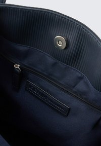 Innenraum der navyblauen Stofftasche mit glatter Textur, ausgestattet mit einer Reißverschlusstasche und einem magnetischen Druckverschluss. Sichtbares geprägt Branding.