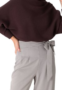 Pull côtelé bordeaux assorti à un pantalon taille haute gris et noir à carreaux avec un détail de nœud à la taille.