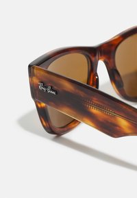 Ochelari de soare Ray-Ban cu o ramă din fâșii de țestoasă, lentile maro și un logo negru pe lateral. Designul este rectangular, cu un finisaj lucios.