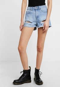 Light blue denim shorts with frayed hem, distressed details, and a button closure. Paired with black lace-up combat boots.