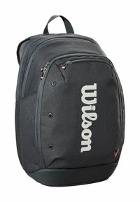Sac à dos en tissu gris avec un grand logo "Wilson" blanc. Offre plusieurs poches zippées et une poignée de transport en haut. Surface texturée.