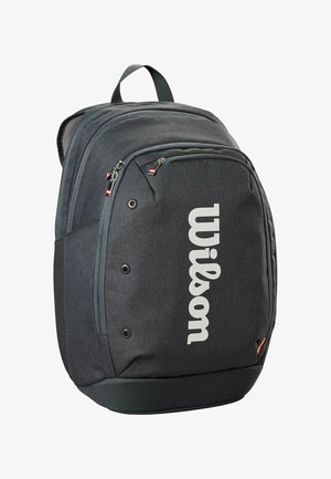 Sac à dos en tissu gris avec un grand logo "Wilson" blanc. Offre plusieurs poches zippées et une poignée de transport en haut. Surface texturée.
