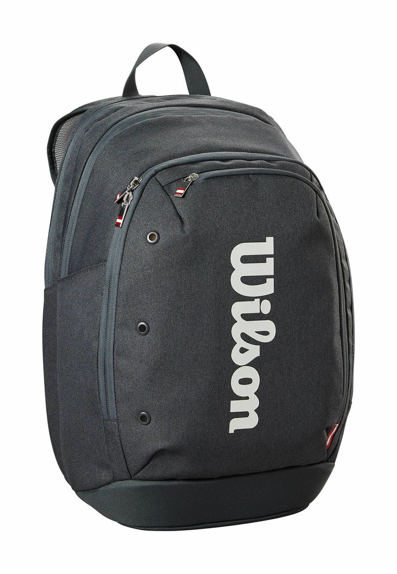 Sac à dos en tissu gris avec un grand logo "Wilson" blanc. Offre plusieurs poches zippées et une poignée de transport en haut. Surface texturée.