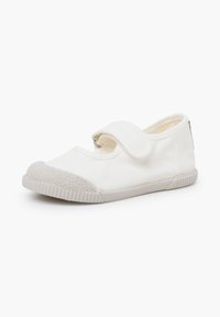 Chaussure en toile blanche pour enfants, avec une bride ajustable à scratch et une semelle en caoutchouc texturée ainsi qu'un embout renforcé.