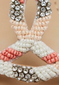 Sandalias con cuentas que presentan cuentas de color coral, rosa pálido y blancas, intercaladas con piedras de strass claras y plateadas sobre una base de color natural.