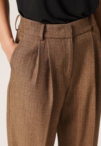 Brązowe spodnie w kant wykonane z teksturowanej tkaniny, z bocznymi kieszeniami i pętlą na pasek w talii, o gładkim wykończeniu i dopasowanym kroju.