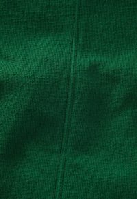 Texturerat mörkgrönt tyg med ribbad yta. Visar en söm som löper vertikalt genom mitten, vilket framhäver materialets väv.