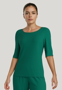 Groene geribbelde top met een bootnek, mouwen tot de elleboog en een zachte textuur, gecombineerd met bijpassende groene broek.