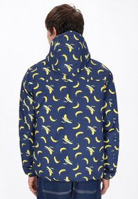 Giacca da marina con cappuccio, caratterizzata da un motivo di banane gialle. Realizzata in materiale leggero e liscio. Polsini elasticizzati ai polsi.