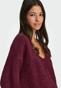 Bordeauxfarbener Pullover mit einer strukturierten, fusseligen Oberfläche, verfügt über einen weiten V-Ausschnitt und lockere Ärmel, gefertigt aus einem weichen, warmen Material.