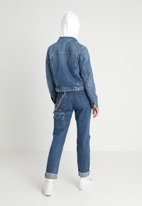 Giacca di denim con una tonalità azzurro chiaro e un design corto, abbinata a jeans strappati coordinati, con un dettaglio a catena sul retro.