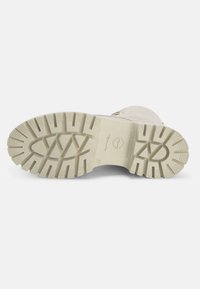 Semelle de botte en caoutchouc beige clair, présentant un motif de bande de roulement robuste pour une meilleure traction. Marquage de la marque et taille "37" sur la base.