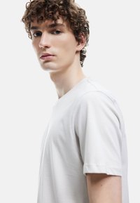 Camiseta gris claro de suave tejido de algodón, con un clásico cuello redondo y mangas cortas, con un corte relajado y detalles de costura mínimos.