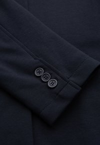 Manche de blazer bleu marine foncé avec trois boutons assortis alignés verticalement près du poignet, montrant des détails de couture fins.