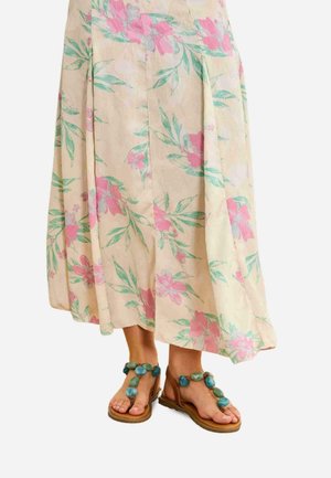 Mujer con una falda floral beige con flores rosas y verdes y sandalias marrones decoradas con grandes piedras turquesas.