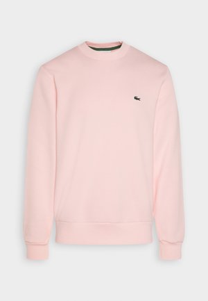 Jasnoróżowa bluza z okrągłym dekoltem, z długimi rękawami i małym czarnym haftowanym logo krokodyla na lewej piersi.