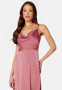 Robe en satin à col bénitier de couleur rose pastel avec des fines bretelles, une silhouette fluide et une texture lisse. Présente un corsage ajusté qui se transforme en jupe.