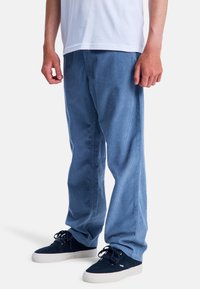 Pantalons en velours côtelé bleu avec une coupe droite, présentant de fines côtes, des poches latérales et portés avec des baskets en suède bleu marine.